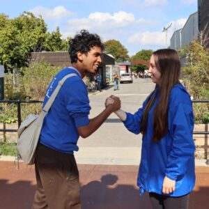 A boy and girl standing palm to palm with blue tops on, standing on top of a bridge.